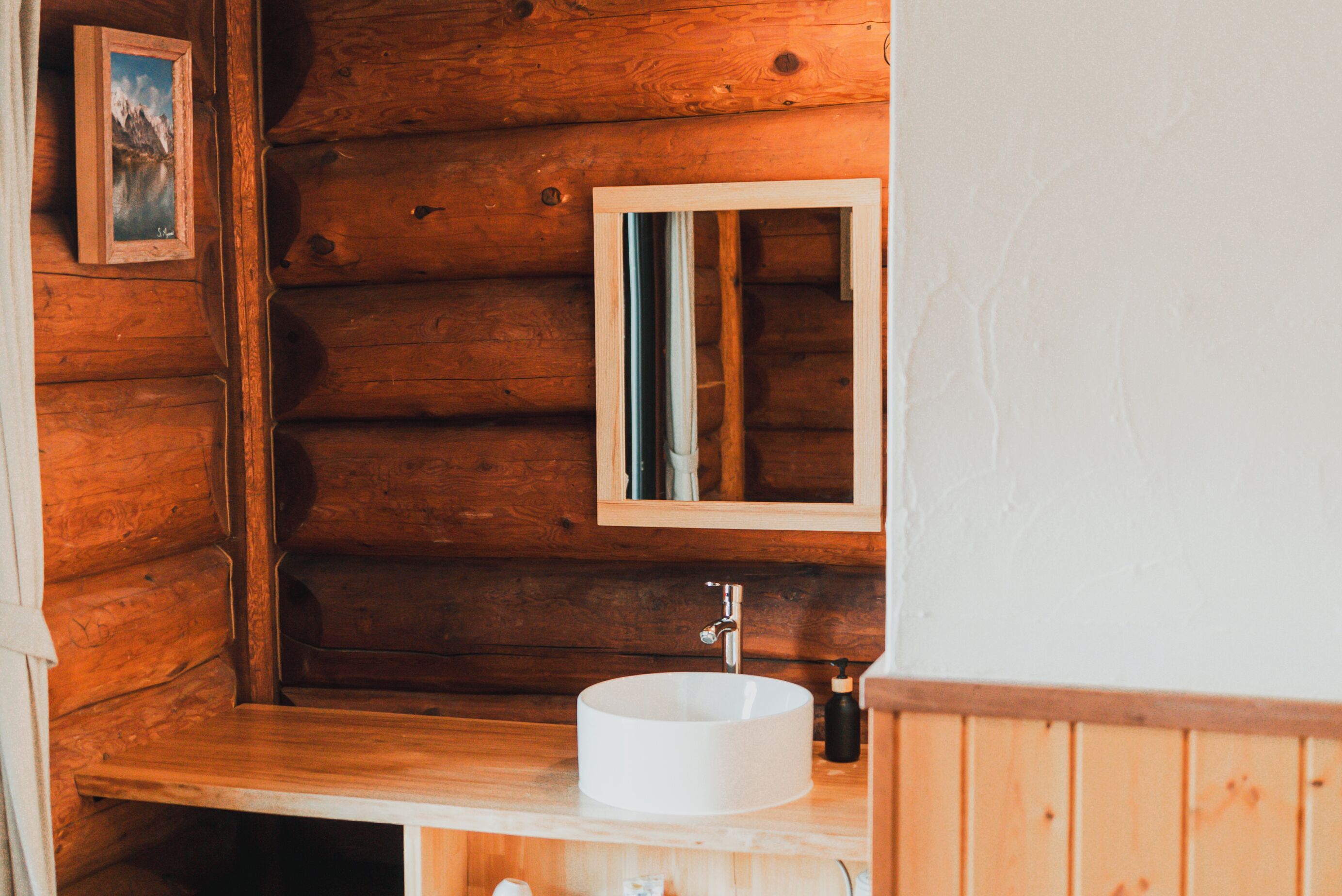 Baño de cabaña de madera con lavabo redondo, espejo y un cuadro en la pared.