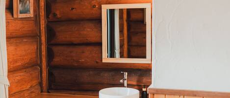 Baño de cabaña de madera con lavabo redondo, espejo y un cuadro en la pared.