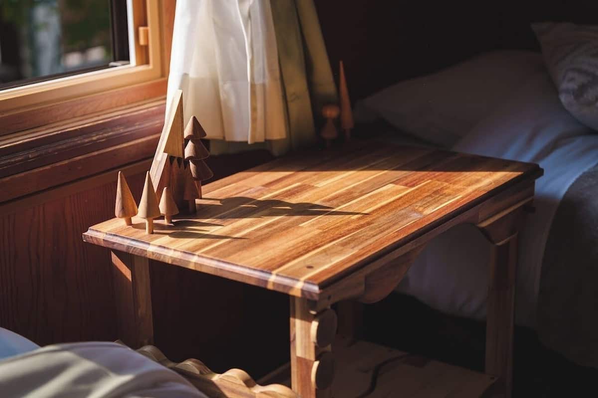 A wooden table with a geometric sculpture, a window with curtains, and a bed with pillows.
