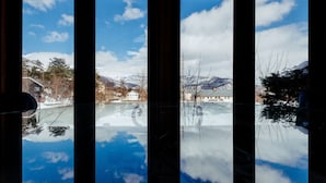 A view through a window with a reflection of a snowy landscape, including mountains and buildings. - Hakuba Pension Meteor (Hakuba)