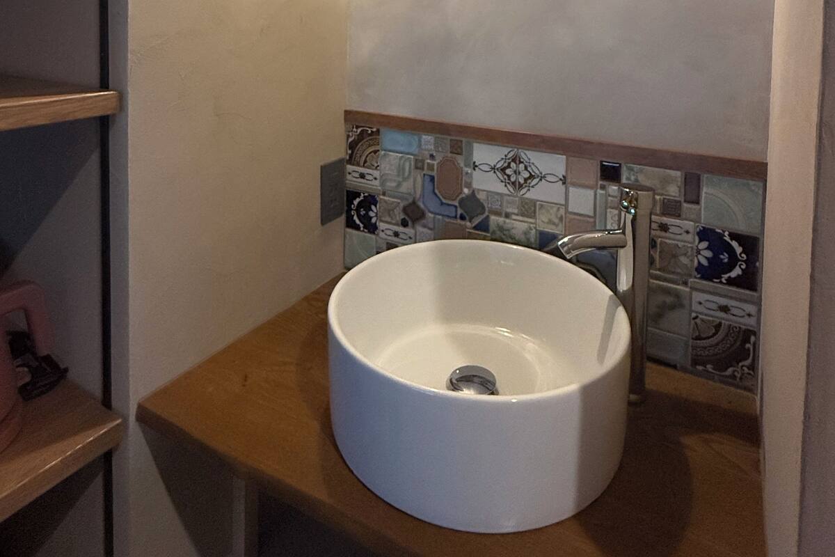 A bathroom with a white sink, a tiled backsplash, and a wooden shelf.