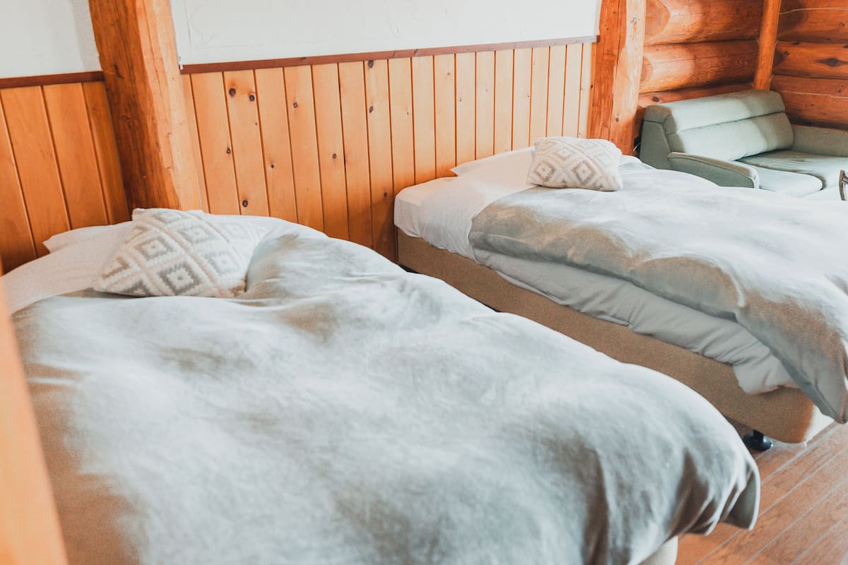 A cabin-style room with two beds, wooden walls, and a green armchair.