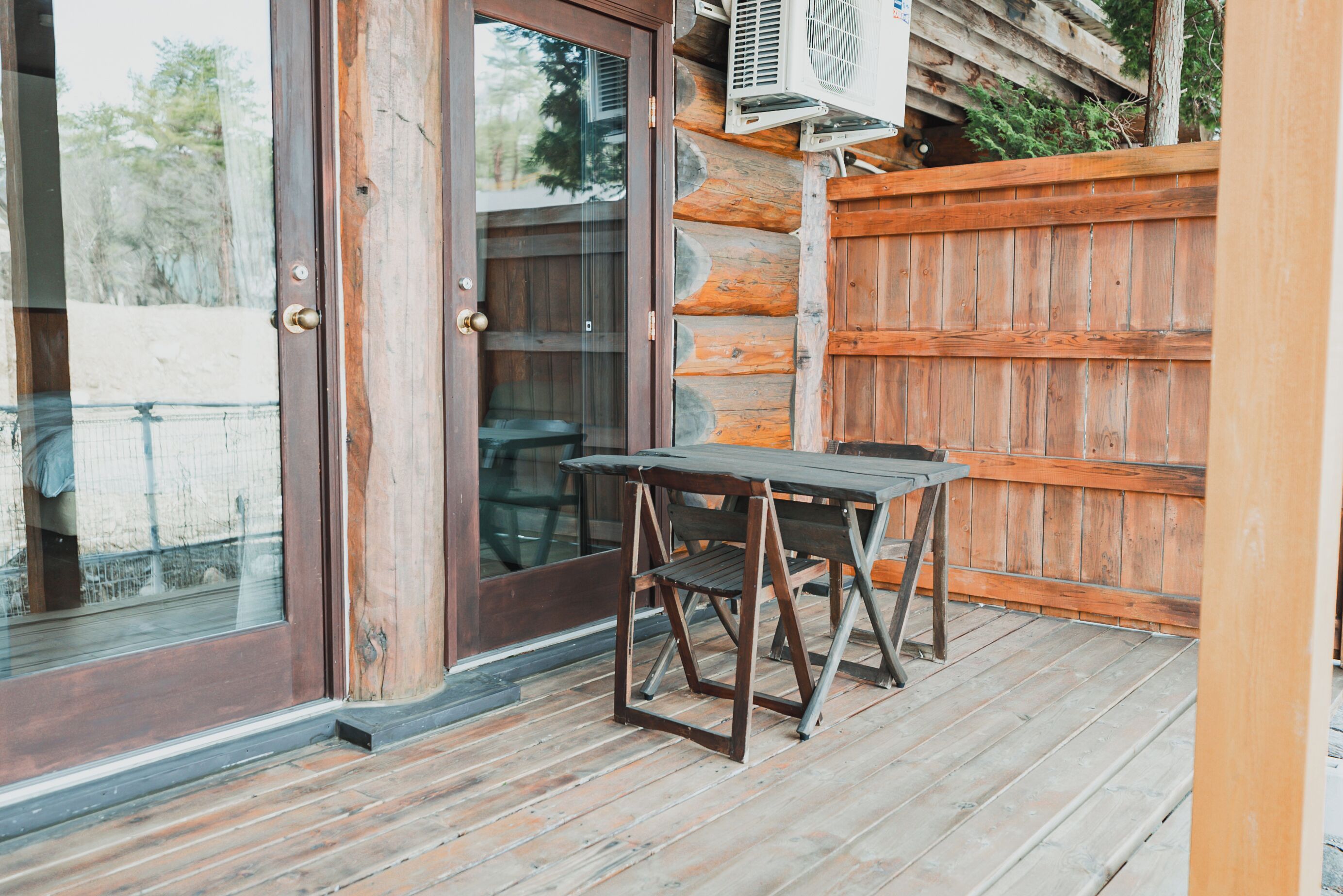 Une terrasse en bois avec une table et des chaises, une porte vitrée et une clôture en bois.