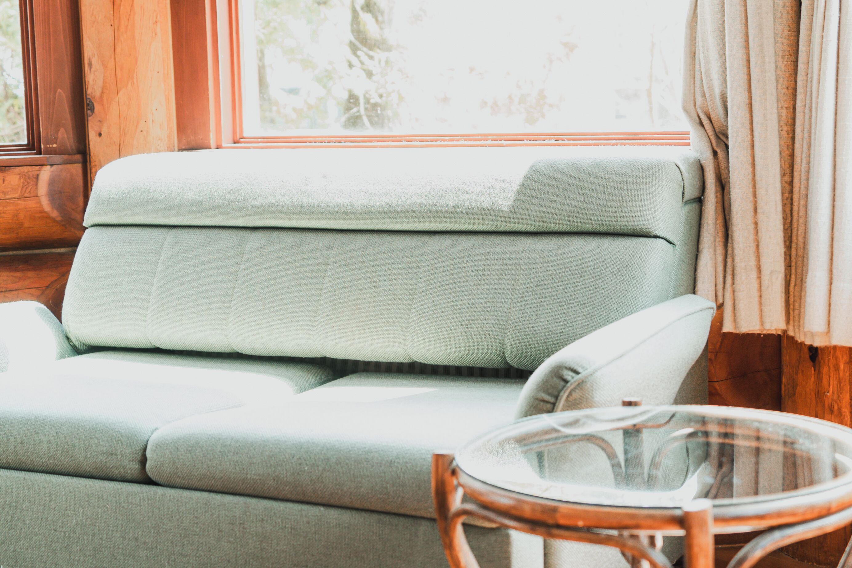 A room with a light green sofa and a glass table.