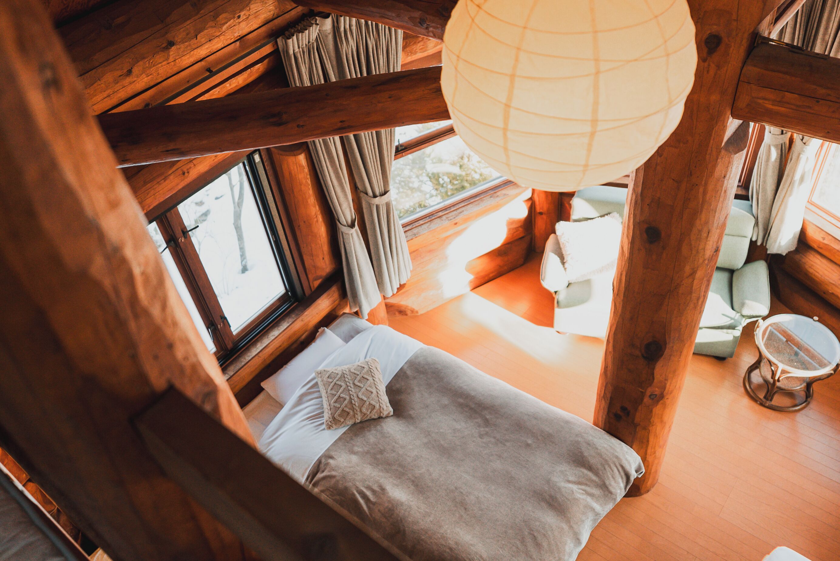 A cozy wooden cabin room with a bed, a hanging light fixture, and a view of the outdoors.