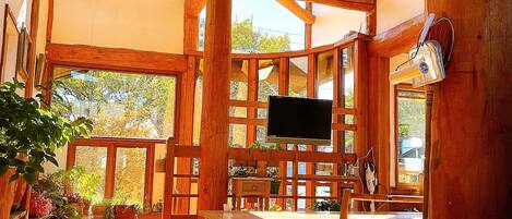 A wooden cabin with a TV, wooden furniture, and large windows.