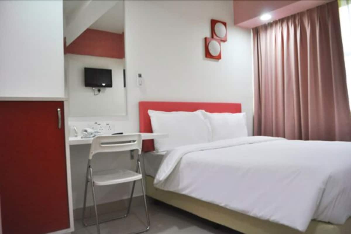 A hotel room with a bed, a desk, a chair, a TV, and a window with curtains.