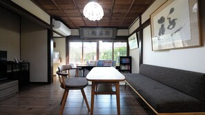 Una habitación tradicional japonesa con suelo de tatami, una mesa baja con sillas, un sofá y una estantería.