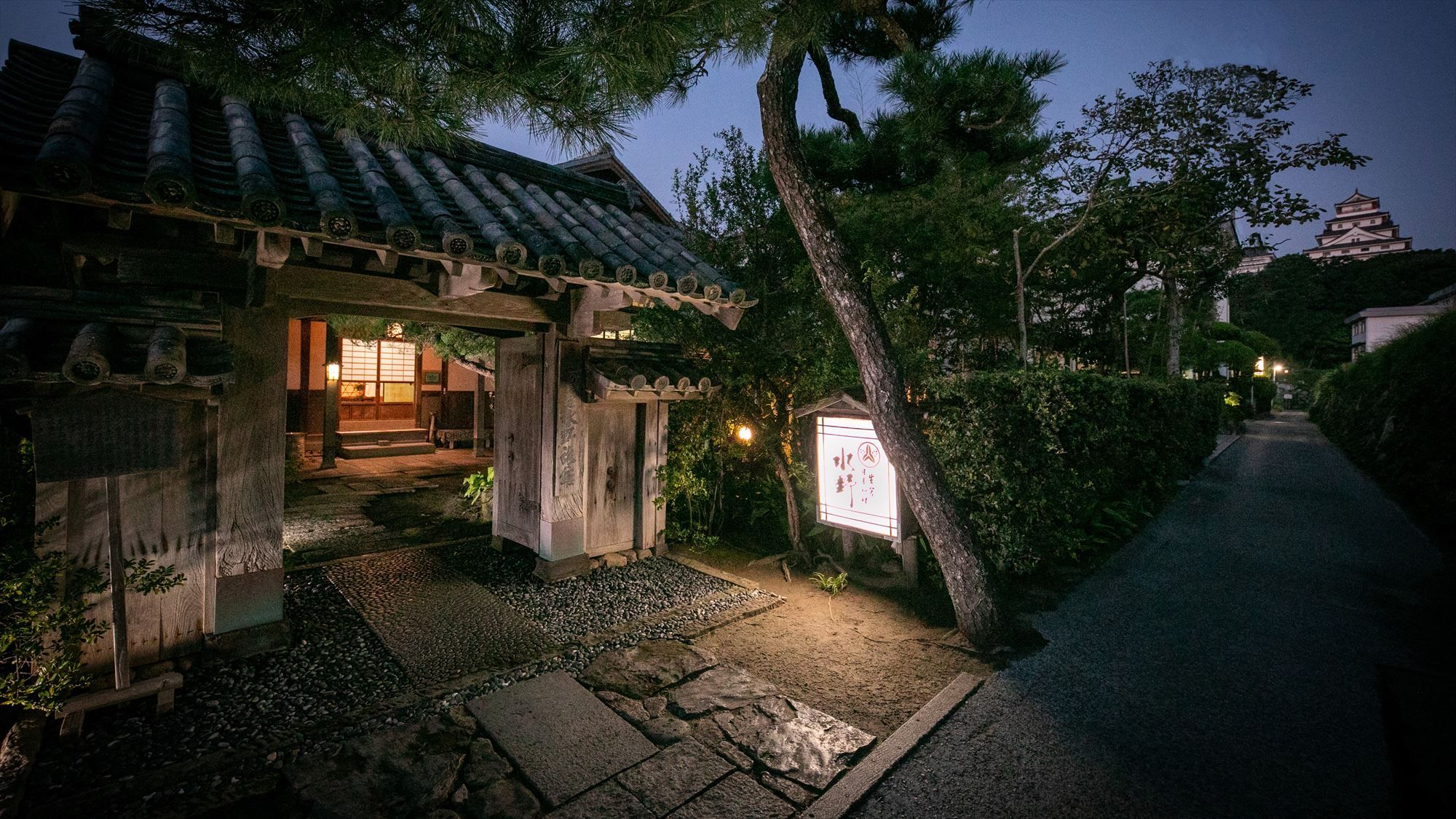 A traditional Japanese building with a tiled roof, stone pathway, and a signboard.