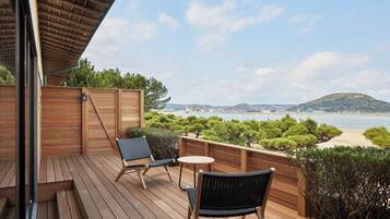 A wooden deck with two chairs and a small table, overlooking a beach and a cityscape.