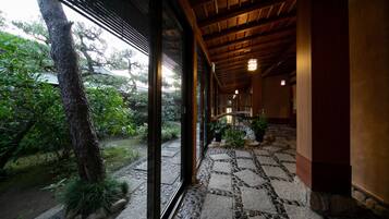 A corridor with a stone-tiled floor leading to a wooden structure with a view of a garden.