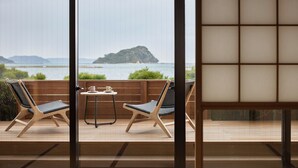 Ein Balkon mit zwei Korbstühlen und einem kleinen Tisch, der auf ein Gewässer und eine ferne Insel blickt.