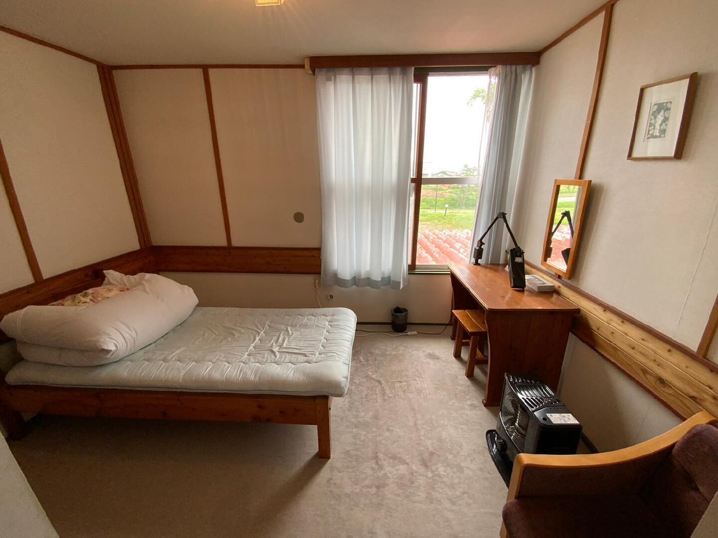 A room with a bed, a desk, a chair, a heater, and a window with curtains.