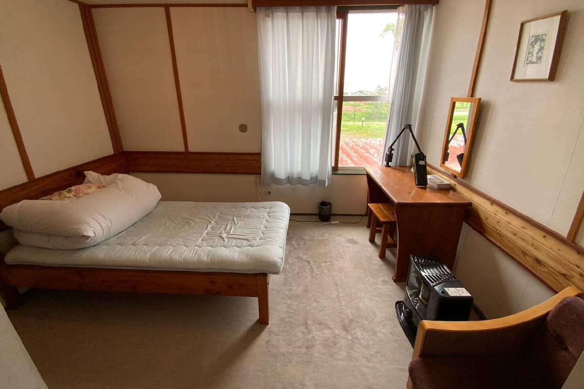 A room with a bed, a desk, a chair, a heater, and a window with curtains.