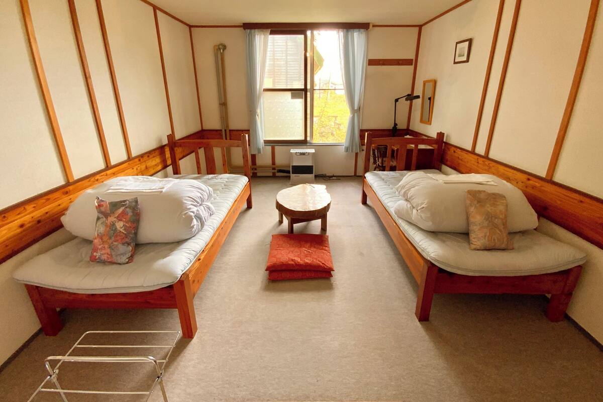 A cozy room with two wooden beds, a small round table, and a window with curtains.