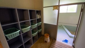 A room with a wooden floor, a window with frosted glass, and a shelf with baskets and bottles. - Mashuko Youth Hostel (Teshikaga)