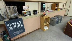 A reception area with a counter, a microwave, a coffee machine, and a sign indicating a 100% classic sushi restaurant. - Mashuko Youth Hostel (Teshikaga)