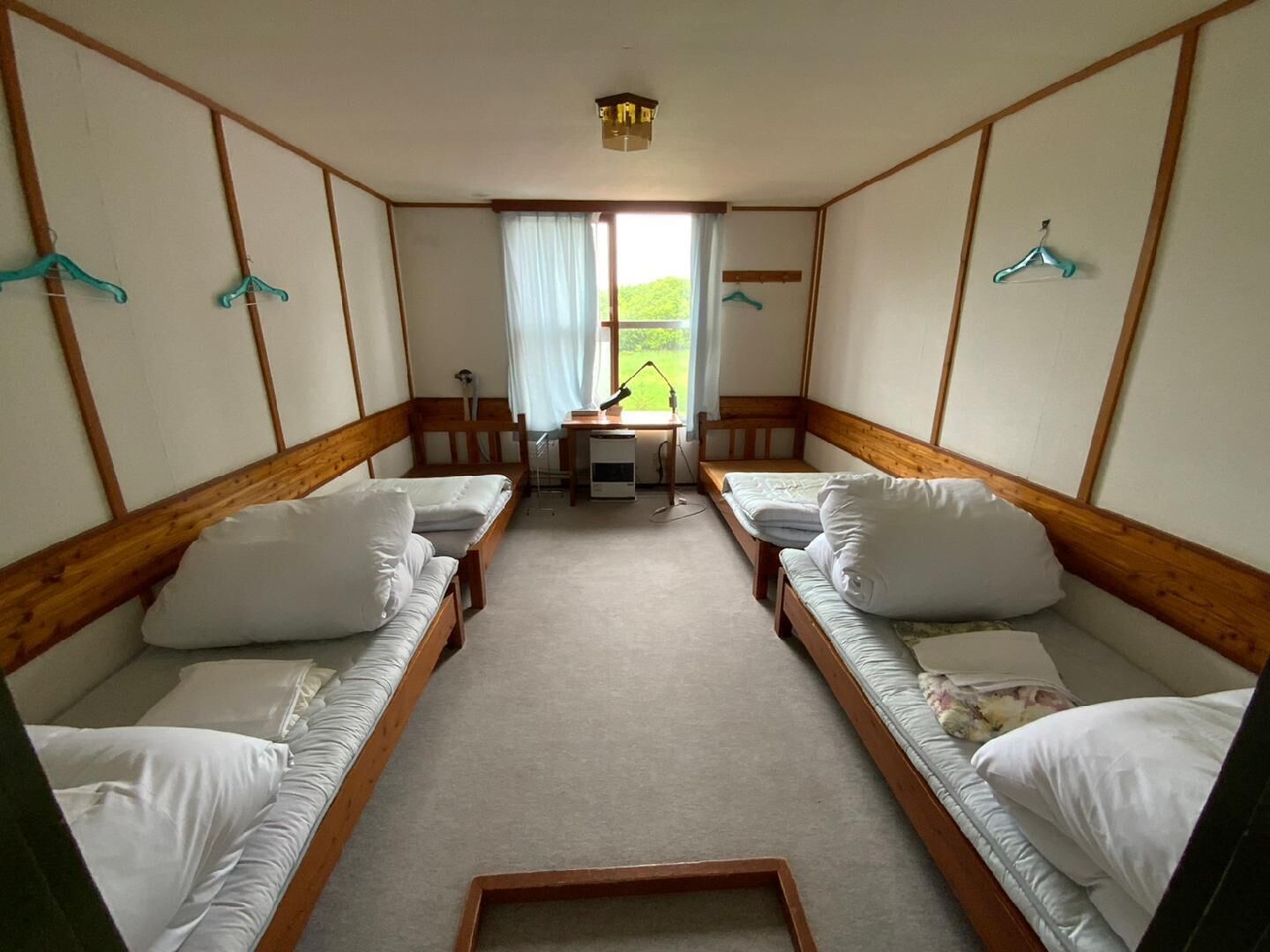 A room with two single beds, a desk, a chair, and a window with curtains.