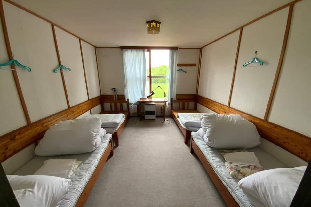 A room with two single beds, a desk, a chair, and a window with curtains.