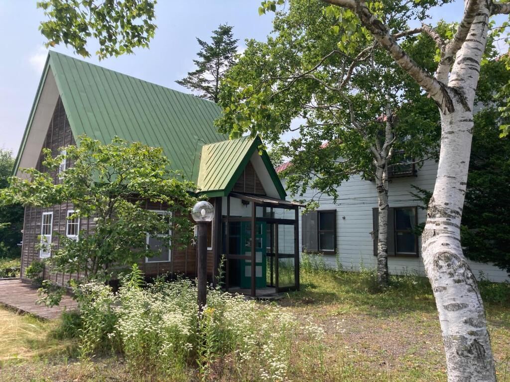 Una casa tradicional con techo verde, un pequeño porche y un árbol en primer plano.