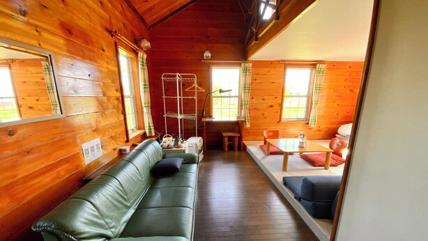 A wooden cabin interior with a green leather sofa, a dining table, and a small kitchen area. - Mashuko Youth Hostel (Teshikaga)