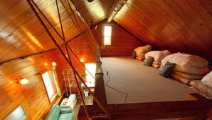 A cozy attic bedroom with a loft bed, a green sofa, and a wooden ceiling. - Mashuko Youth Hostel (Teshikaga)