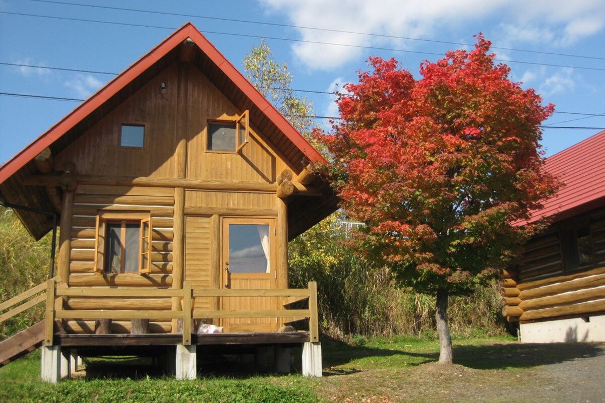 A wooden log cabin with a red roof, a small porch, and a window.