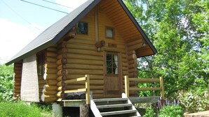 A log cabin with a wooden front door, a small porch, and a set of stairs leading up to the entrance. - Log Cottage Himawari (Nakafurano)