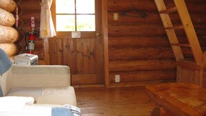 A log cabin interior with a wooden door, a window, a fire extinguisher, a power outlet, and a wooden ladder. - Log Cottage Himawari (Nakafurano)