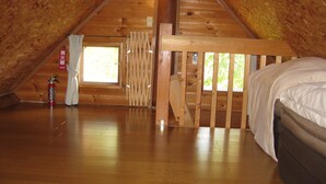 A wooden attic bedroom with a bed, a window, and a fire extinguisher. - Log Cottage Himawari (Nakafurano)