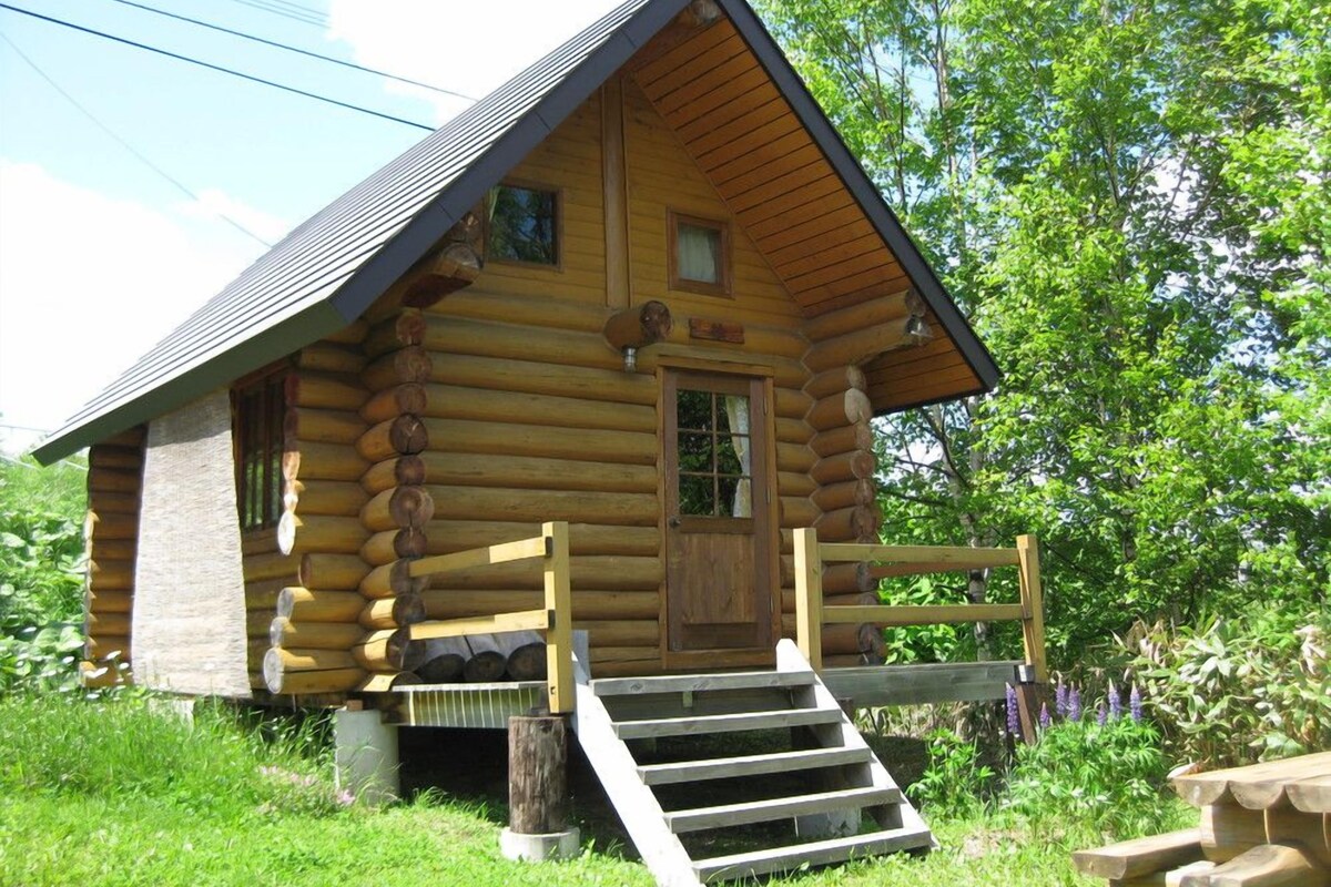 A log cabin with a wooden porch, a front door, and a set of stairs leading up to the entrance.