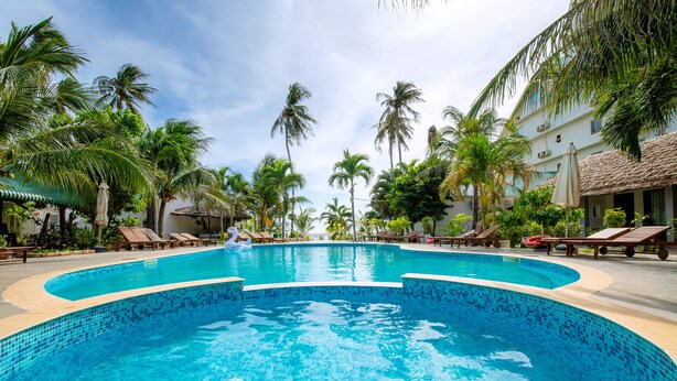 A swimming pool with tiled edges, surrounded by palm trees and lounge chairs.