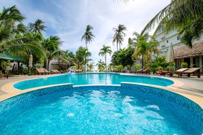 A swimming pool with tiled edges, surrounded by palm trees and lounge chairs.