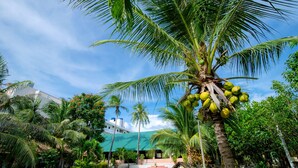 A tropical resort with palm trees, a pool, and a building with a green roof.