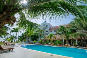 A pool area with lounge chairs, a palm tree, and a building with a red roof.