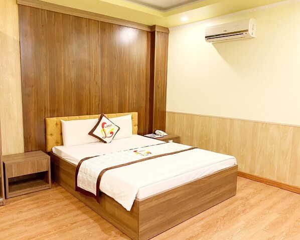 A hotel room with a wooden bed, a bedside table, and an air conditioning unit on the wall. - Linh Phuong 8 Hotel (Can Tho)