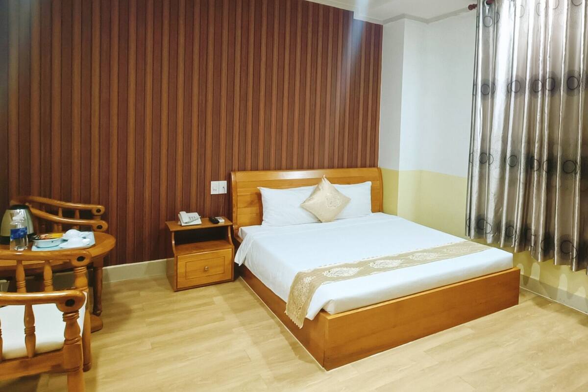 A hotel room with a wooden bed, a wooden nightstand, a wooden dresser, a wooden chair, and a wooden desk.