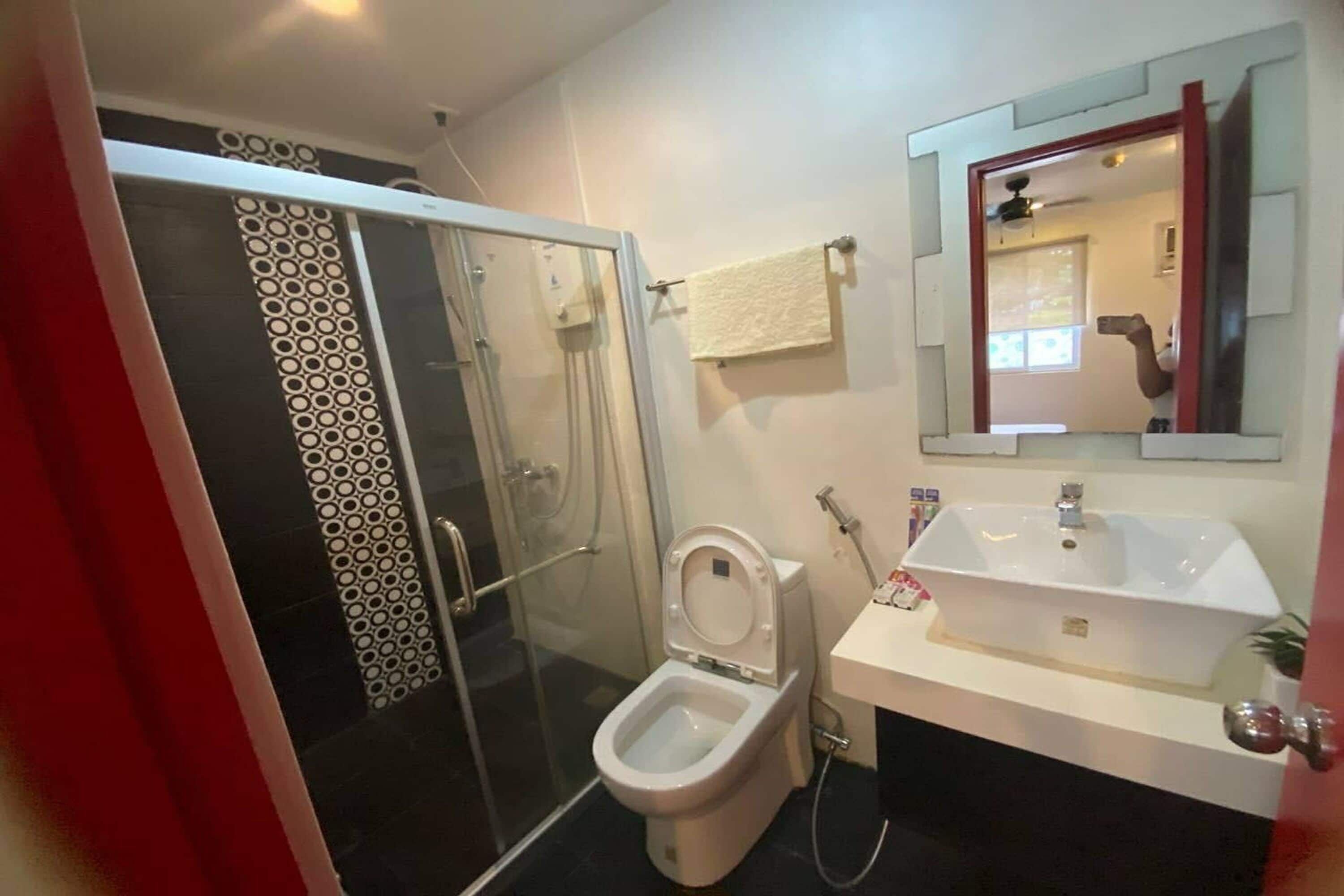 A bathroom with a glass-enclosed shower, a white toilet, a sink, and a mirror.