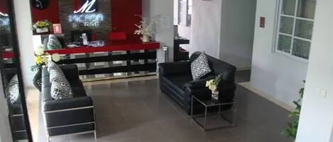 Un moderno vestíbulo de hotel con una recepción, un sofá negro y una pequeña mesa con un jarrón de flores.