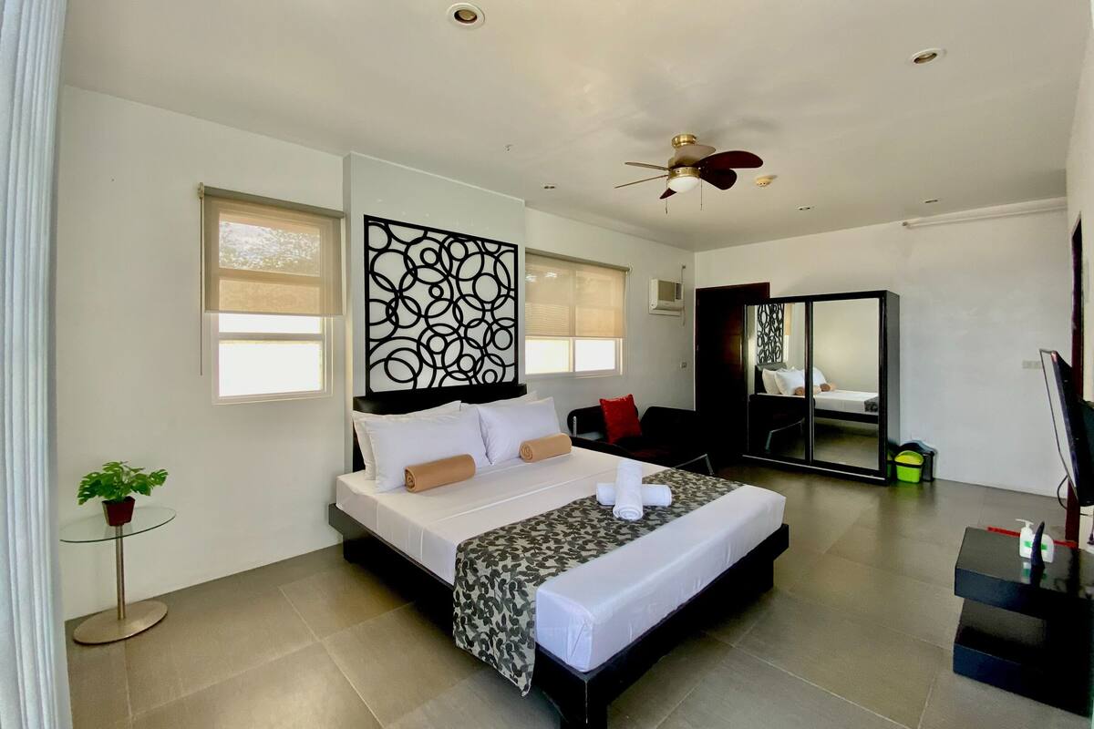 A modern hotel room with a large bed, a ceiling fan, and a large mirror.