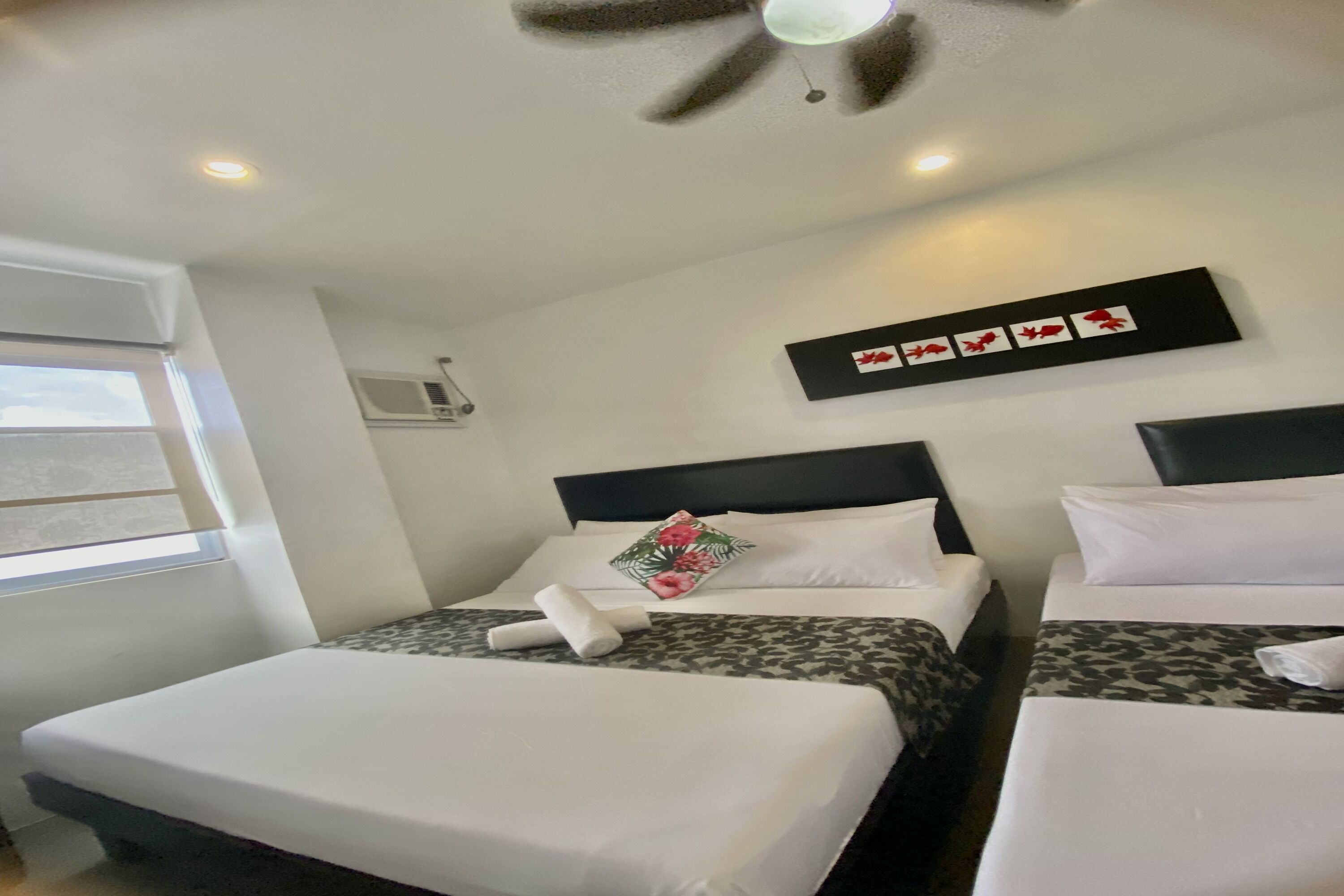 Quarto de hotel com duas camas, um ventilador de teto, uma janela e ar-condicionado fixado na parede.
