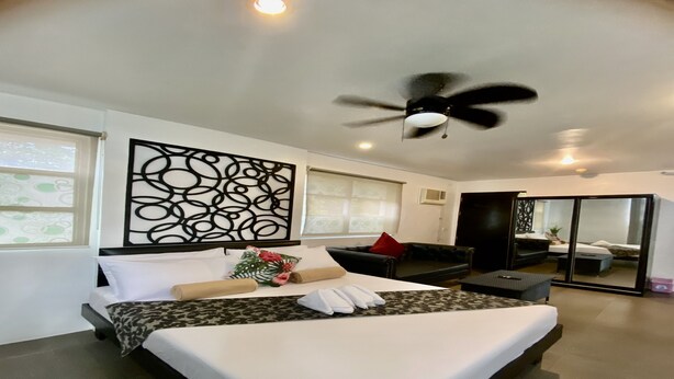 A modern hotel room with a large bed, a ceiling fan, a decorative wall panel, a sofa, and a sliding glass door leading to a balcony. - Micasa Lodge Palawan (Coron)