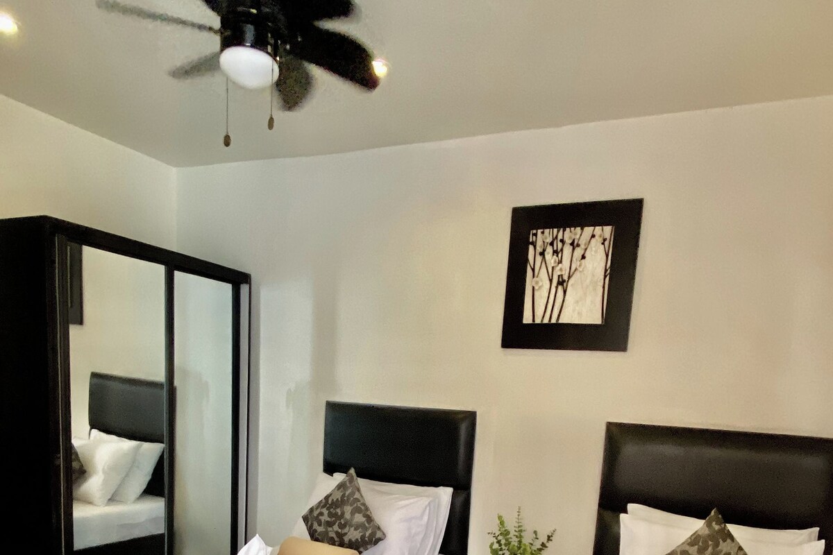 Une chambre d’hôtel avec deux lits, un ventilateur de plafond, un miroir et une œuvre d’art encadrée au mur.
