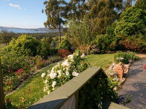 A garden with a wooden deck, various flowering plants, and a view of a lake and hills. - Waterview Gardens B&B (Margate)