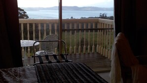 A room with a bed, a chair, and a view of a balcony with a railing and a table. - Waterview Gardens B&B (Margate)