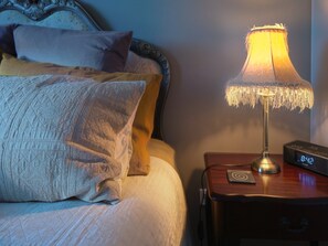 A neatly made bed with a patterned bedspread and pillows, a bedside table with a lamp and a digital clock, and a wall with a decorative headboard. - Waterview Gardens B&B (Margate)