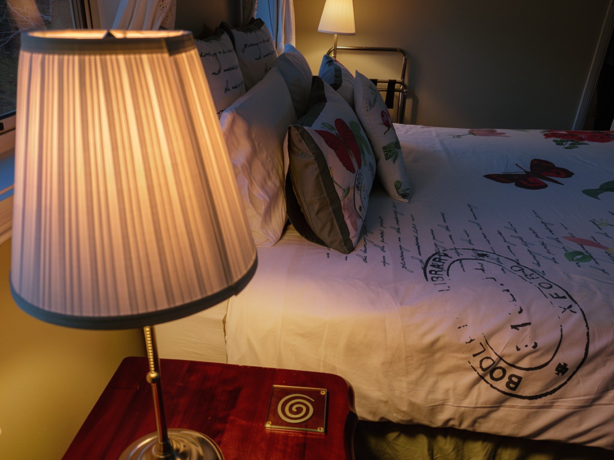 A bed with a floral comforter, a lamp on a bedside table, and a wall-mounted nightstand.