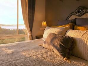 A bedroom with a large window, a bed with multiple pillows, and a lamp on a bedside table. - Waterview Gardens B&B (Margate)