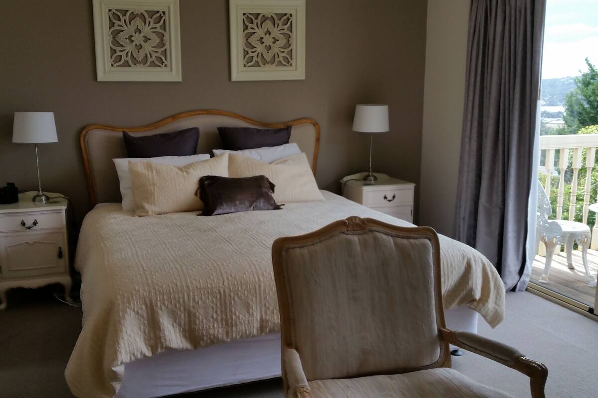 A bedroom with a large bed, two bedside tables, a chair, and a balcony view.