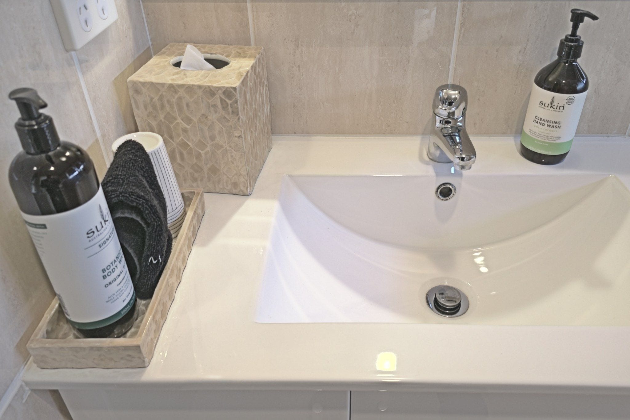 A bathroom sink with a tissue box, a bottle of hand soap, and a bottle of body wash.